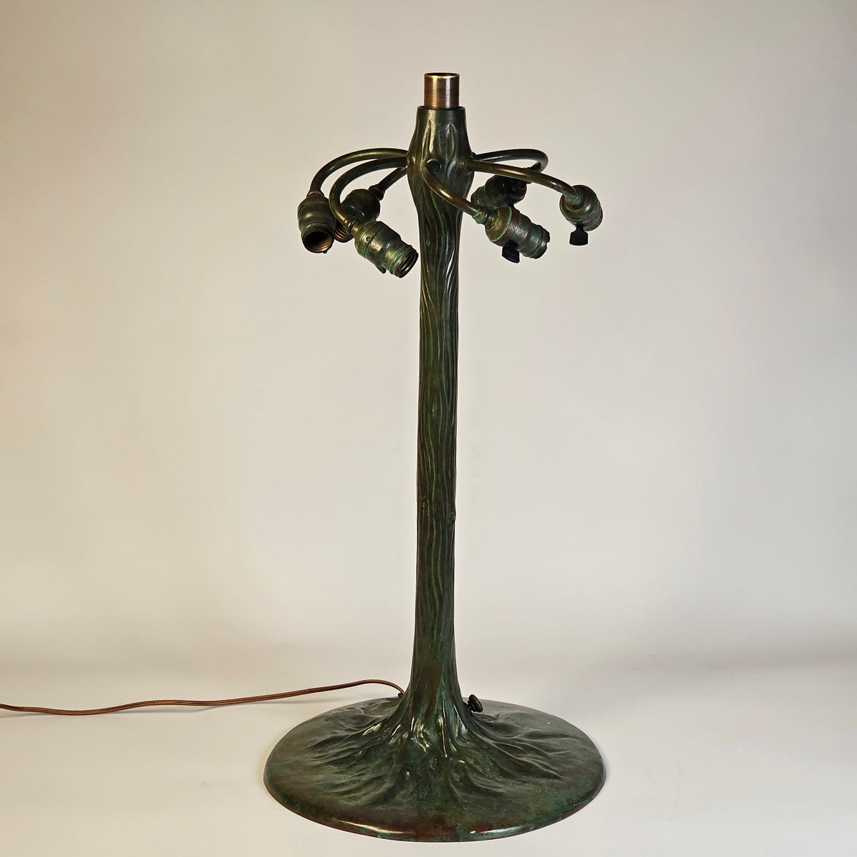 lamp base with a textured, tree-like trunk and three curved arms ending in bulb sockets, mounted to a circular backplate on a plain off-white wall.