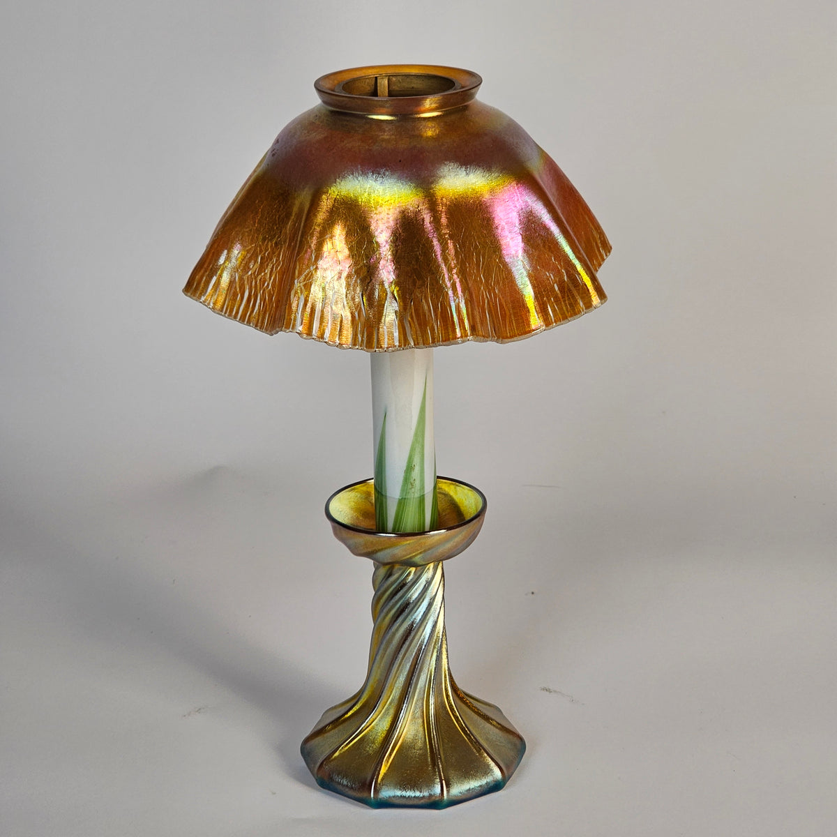 An iridescent gold glass wall sconce with a flared shade, a twisted stem, and a white glass candle-style bulb, shown against a plain light gray background.